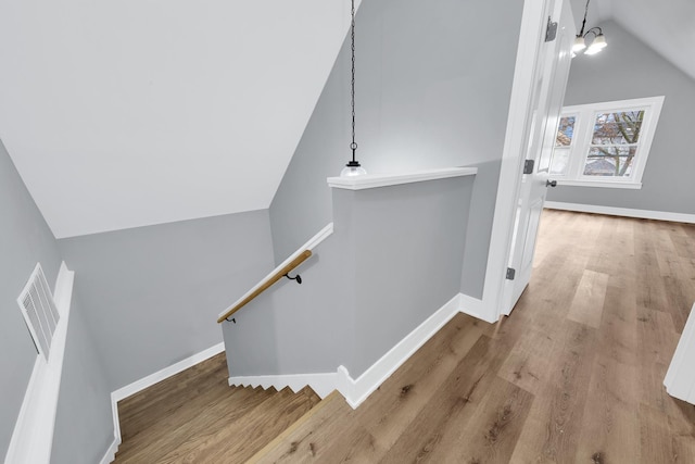 stairs with vaulted ceiling, wood finished floors, visible vents, and baseboards