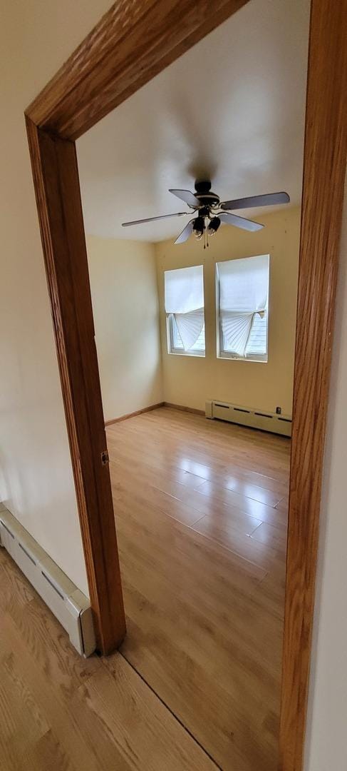 unfurnished room featuring a baseboard heating unit, light wood-style flooring, and ceiling fan