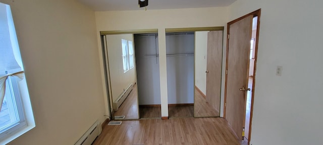 unfurnished bedroom with light wood-type flooring, multiple closets, baseboards, and a baseboard radiator