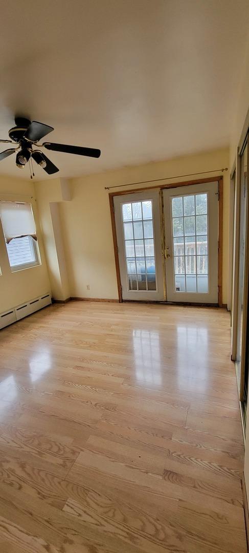 unfurnished room featuring light wood finished floors, a ceiling fan, a wealth of natural light, and a baseboard radiator