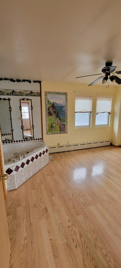 interior space featuring a baseboard heating unit, a ceiling fan, and light wood finished floors