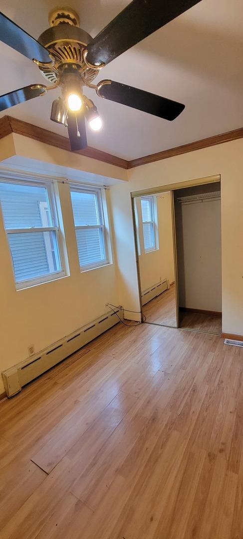 unfurnished bedroom featuring light wood-style flooring, crown molding, a ceiling fan, and a baseboard radiator