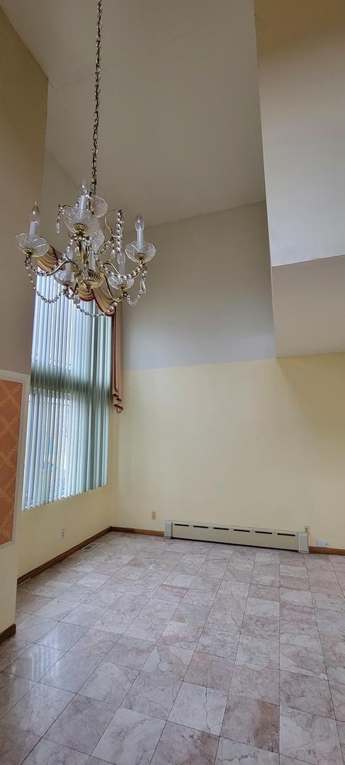 unfurnished room featuring a baseboard heating unit, an inviting chandelier, a high ceiling, and baseboards