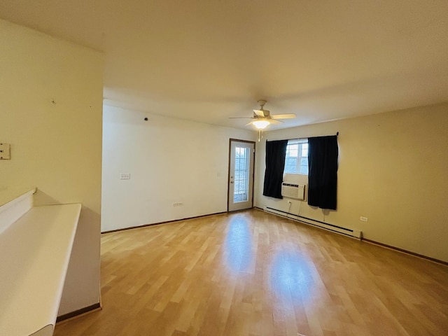 spare room featuring a baseboard heating unit, light wood-type flooring, ceiling fan, and baseboards