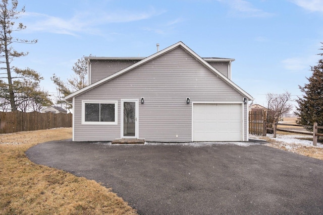 view of side of home featuring aphalt driveway, an attached garage, and fence