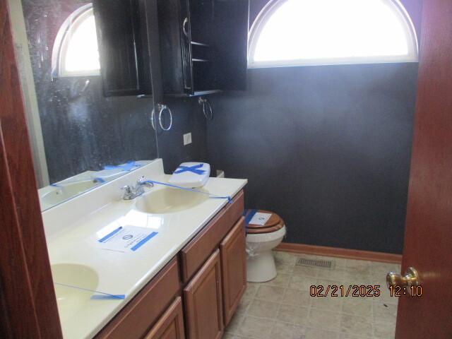 bathroom with double vanity, visible vents, toilet, a sink, and baseboards