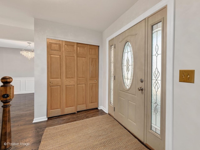 entrance foyer with a notable chandelier, dark wood-style floors, wainscoting, and a decorative wall