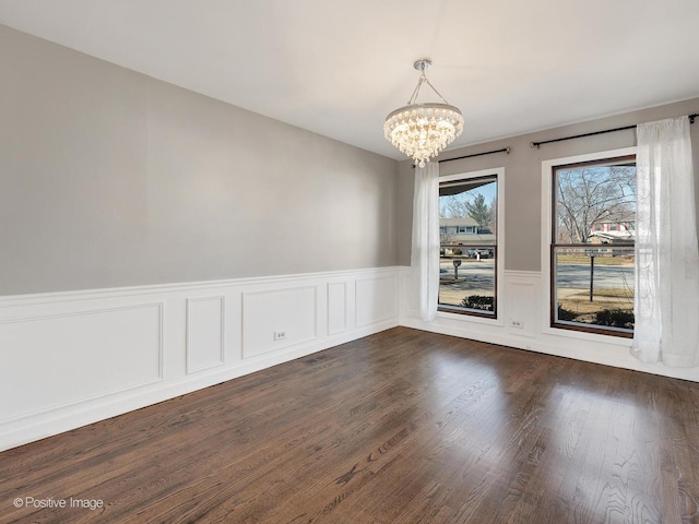 unfurnished dining area featuring a notable chandelier, a wainscoted wall, and dark wood-style flooring