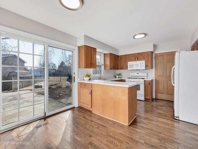 kitchen with white appliances, a peninsula, dark wood-style flooring, and light countertops