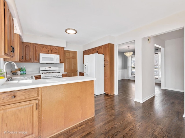 kitchen featuring light countertops, a peninsula, dark wood-style floors, white appliances, and a sink