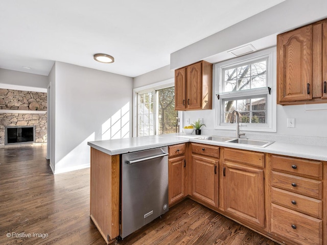 kitchen featuring a sink, a peninsula, a stone fireplace, dishwasher, and dark wood-style flooring