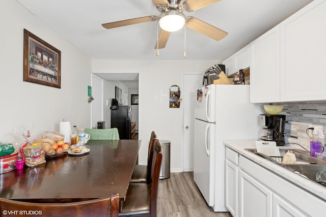 kitchen with tasteful backsplash, light countertops, freestanding refrigerator, white cabinetry, and light wood-type flooring