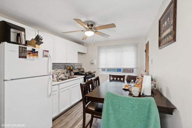 kitchen featuring a sink, white cabinetry, stainless steel range with gas cooktop, freestanding refrigerator, and tasteful backsplash