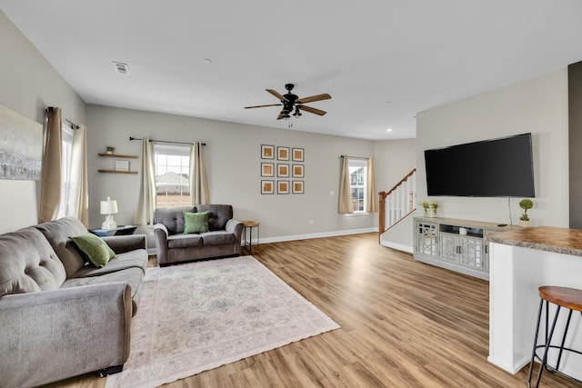 living room with stairs, light wood finished floors, visible vents, and baseboards