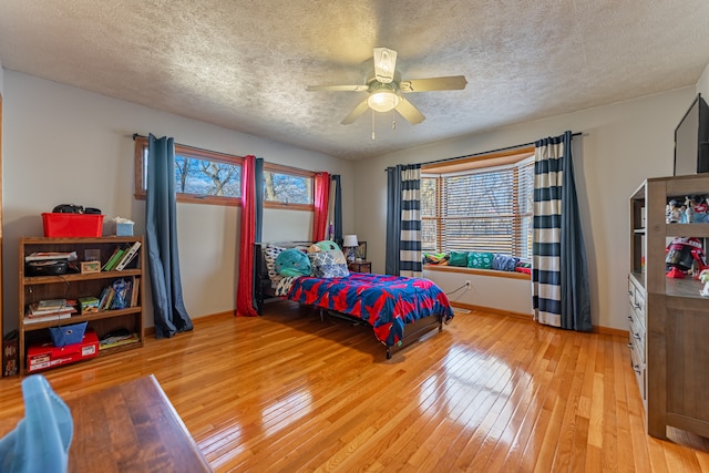 bedroom with light wood finished floors, ceiling fan, baseboards, and a textured ceiling