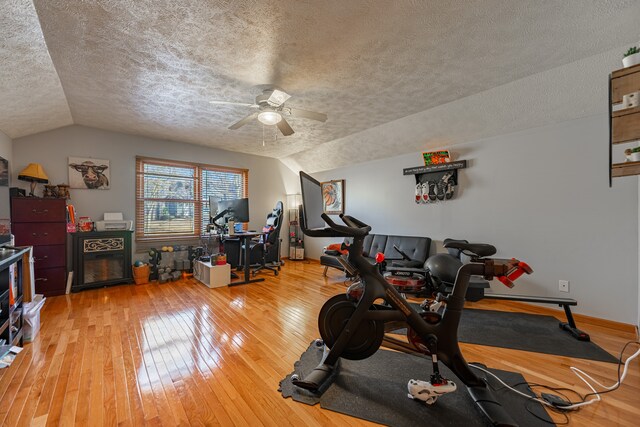 exercise area featuring light wood-type flooring, a textured ceiling, vaulted ceiling, and a ceiling fan