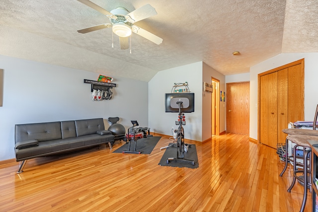 exercise area featuring vaulted ceiling, ceiling fan, a textured ceiling, and light wood-style flooring