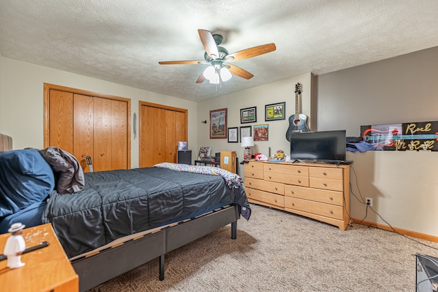 bedroom featuring two closets, light colored carpet, a ceiling fan, a textured ceiling, and baseboards