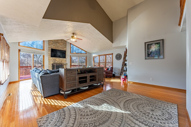 living room with wood-type flooring, high vaulted ceiling, ceiling fan, and a stone fireplace