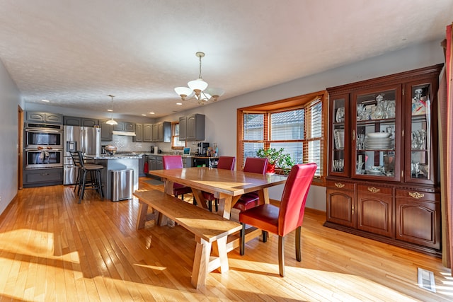 dining area featuring a chandelier, visible vents, light wood-style flooring, and a textured ceiling