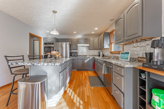 kitchen featuring gray cabinets, decorative backsplash, appliances with stainless steel finishes, light wood-style floors, and under cabinet range hood