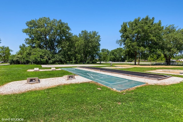 view of home's community with shuffleboard, a yard, and view of wooded area