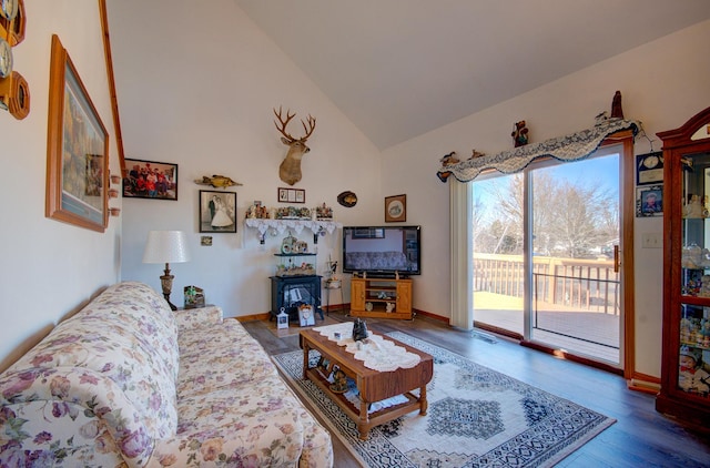 living area with wood finished floors, high vaulted ceiling, and a wood stove