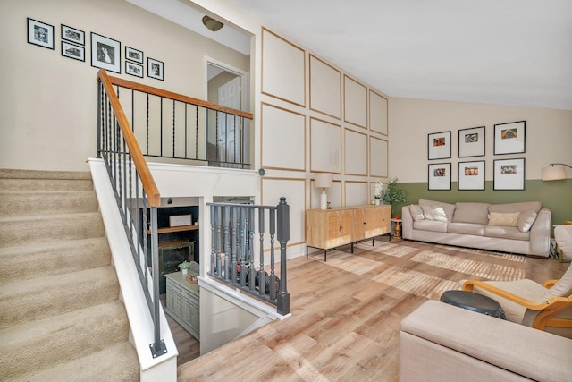 living area featuring high vaulted ceiling, light wood-style flooring, stairway, and a glass covered fireplace