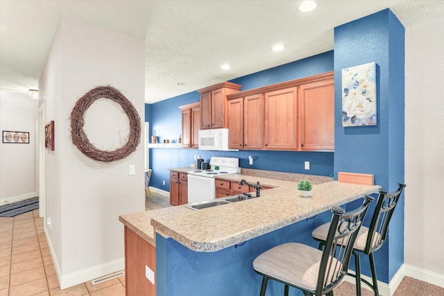 kitchen with white appliances, visible vents, light countertops, a kitchen bar, and brown cabinets