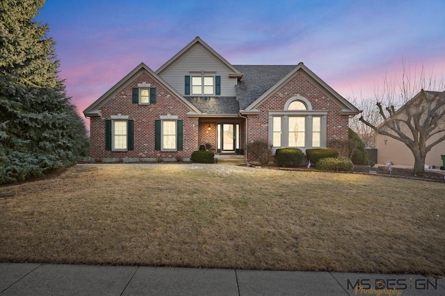 traditional-style home with brick siding, a front yard, and roof with shingles