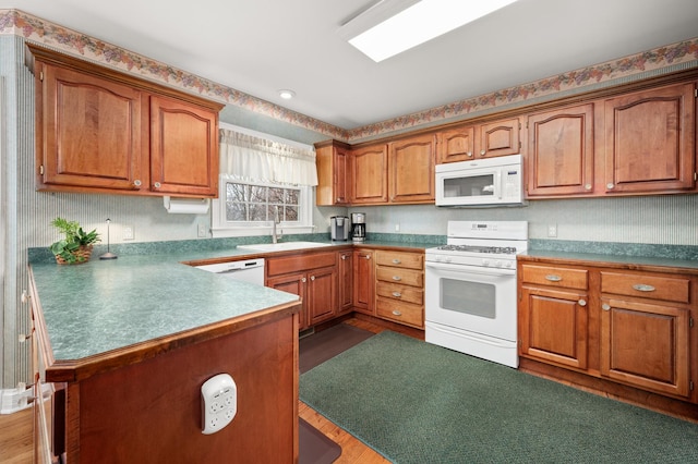 kitchen with white appliances, brown cabinetry, a peninsula, a sink, and dark wood-type flooring