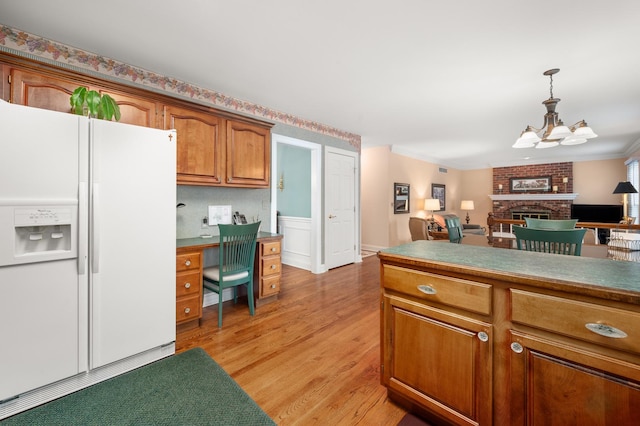 kitchen featuring brown cabinetry, a fireplace, white refrigerator with ice dispenser, pendant lighting, and light wood-type flooring