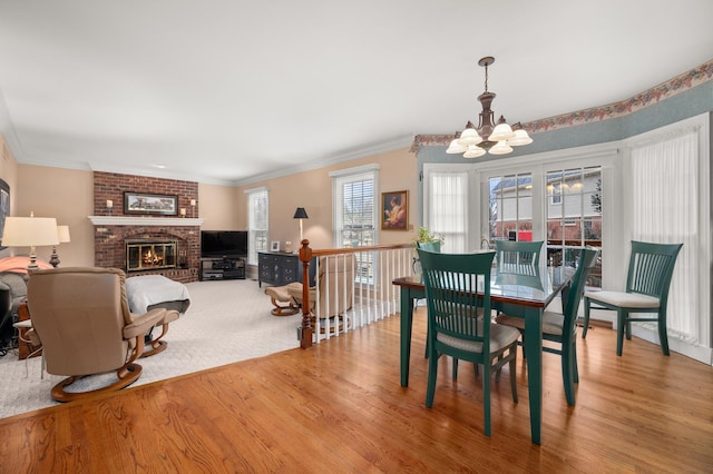 dining space featuring crown molding, a brick fireplace, wood finished floors, and a chandelier