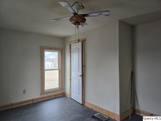 spare room with a ceiling fan, visible vents, baseboards, and wood finished floors