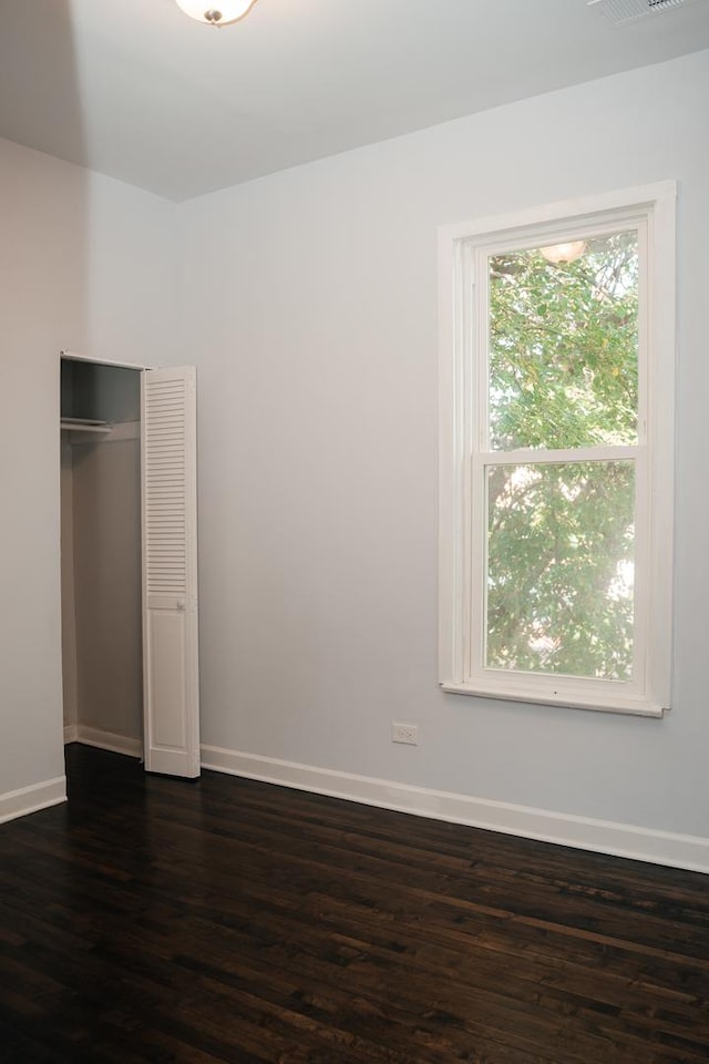 unfurnished bedroom with dark wood-style flooring, multiple windows, a closet, and baseboards