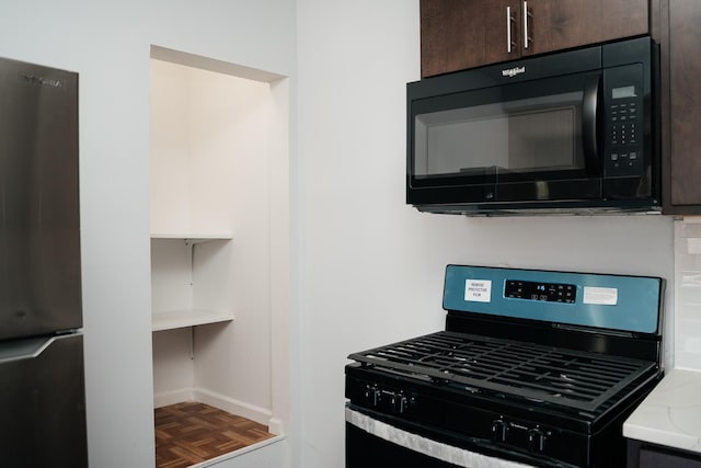 kitchen featuring black microwave, stainless steel gas range oven, dark brown cabinetry, baseboards, and freestanding refrigerator