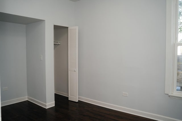 unfurnished bedroom with dark wood-type flooring, a closet, and baseboards