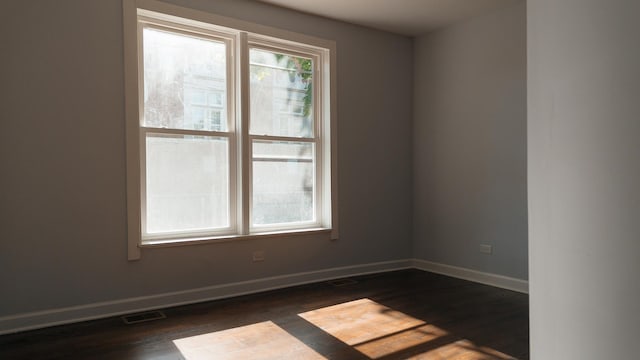 spare room with dark wood-style floors, visible vents, and baseboards