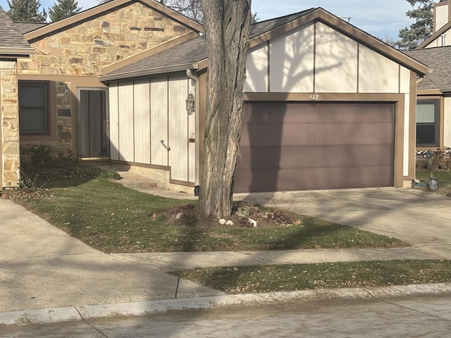 view of side of property featuring a garage, stone siding, a shingled roof, and concrete driveway