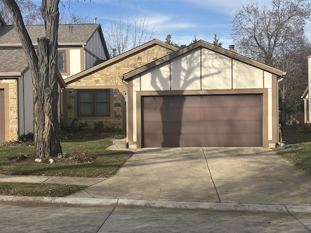 tudor-style house with an attached garage, stone siding, a shingled roof, and concrete driveway