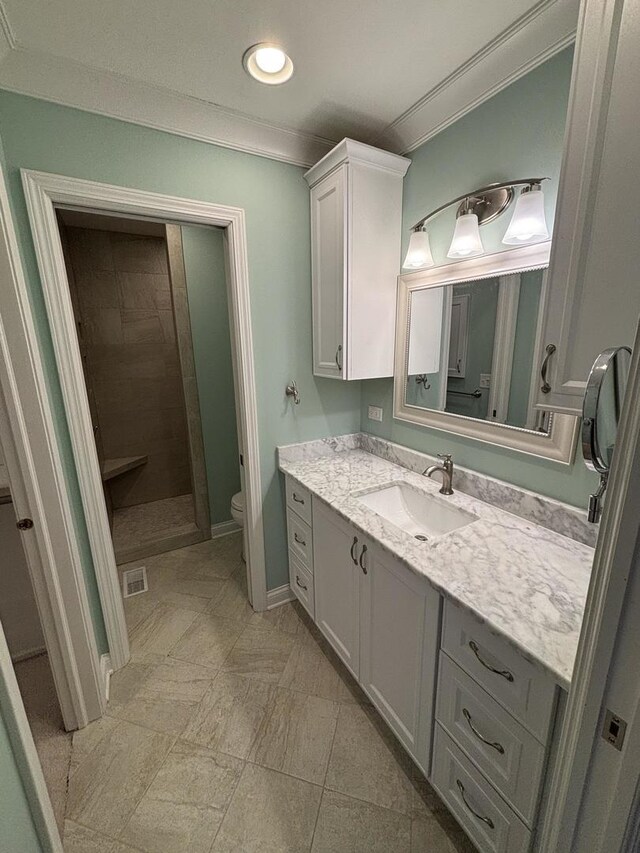 full bath with toilet, vanity, baseboards, ornamental molding, and tiled shower