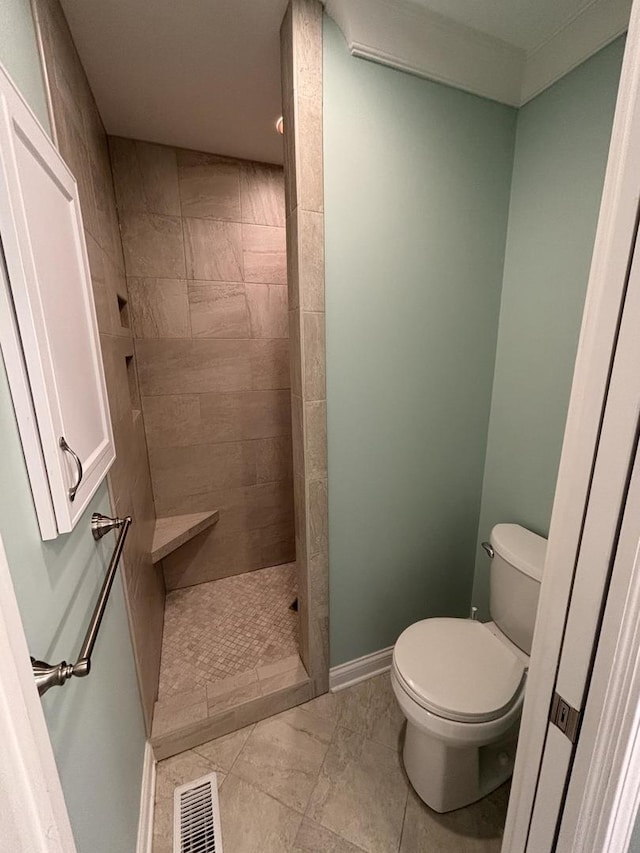 full bath featuring toilet, a tile shower, visible vents, and baseboards