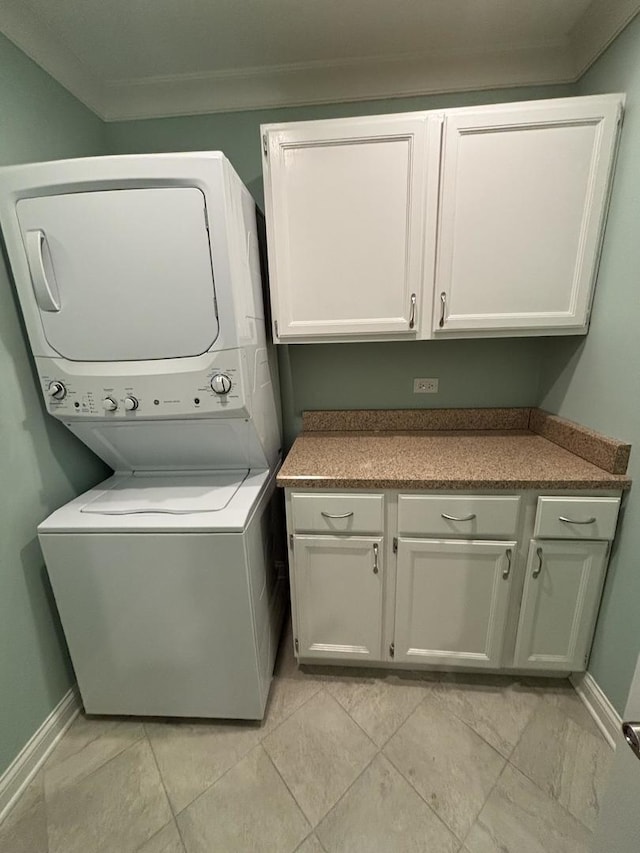 washroom featuring ornamental molding, cabinet space, stacked washer and clothes dryer, and baseboards