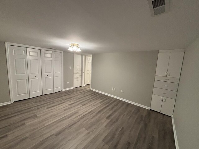 unfurnished bedroom with a closet, dark wood-style flooring, visible vents, and baseboards