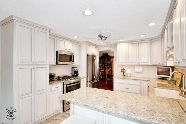 kitchen with ceiling fan, stainless steel appliances, a peninsula, a sink, and light stone countertops