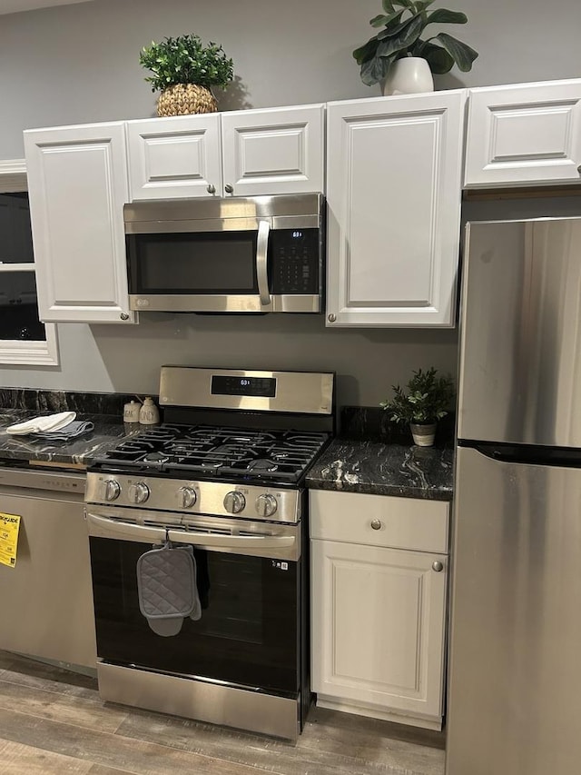 kitchen featuring stainless steel appliances, wood finished floors, white cabinets, and dark stone counters