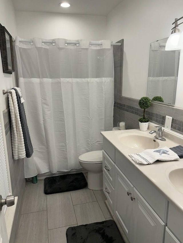 bathroom with curtained shower, toilet, double vanity, tile walls, and a sink