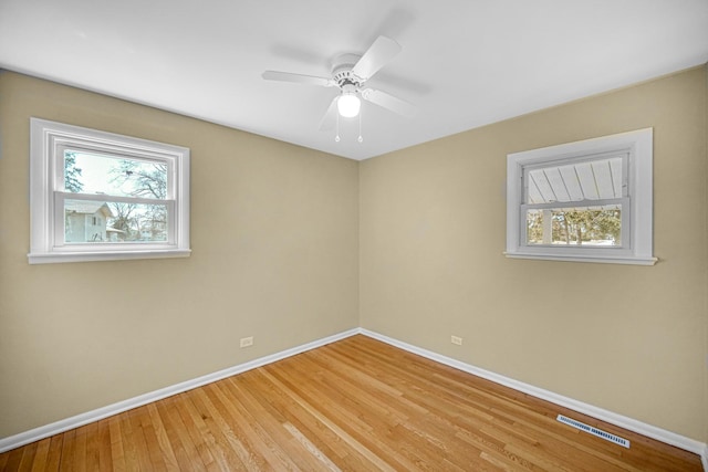 empty room with light wood finished floors, a wealth of natural light, visible vents, and baseboards