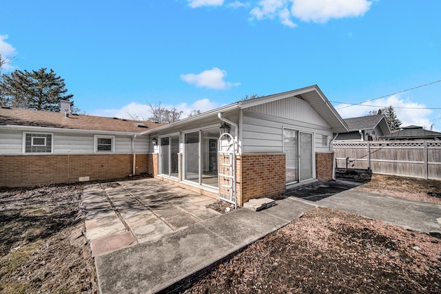 back of house featuring a patio, brick siding, fence, and a sunroom