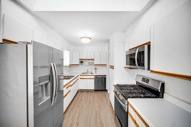 kitchen with stainless steel appliances, light countertops, light wood-style floors, white cabinets, and a sink